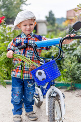 a child rides a bicycle with a basket for transporting vegetables, in which there is a carrot from the garden