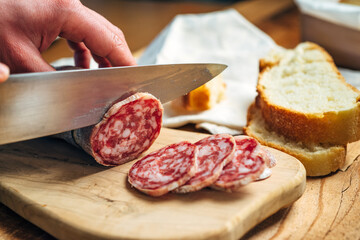 Salami being cut into slices on the wooden cutting board
