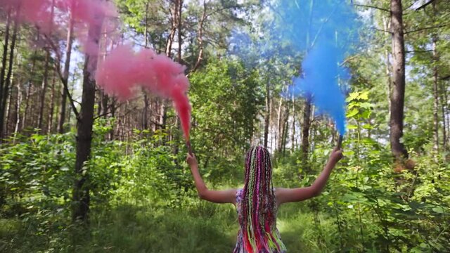 A teenager girl with colored smoke walks in the forest.