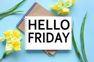 Hello Friday. text on white notepad paper on blue background. near notepad with yellow flowers and green leaves