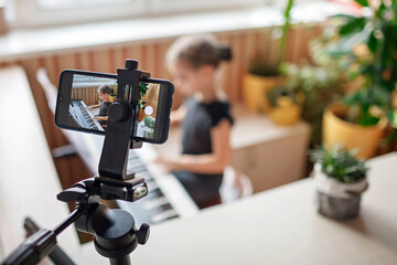 Pretty young musician in classic black dress playing digital piano at home during online concert and recording video, social distance during quarantine, online education concept, video blogging