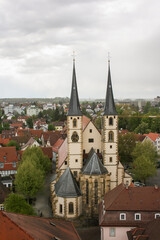 Fototapeta premium Bad Wimpfen church, cloistered between the red-roofed half-timbered houses, with two symmetrical pointed towers on a cloudy day.