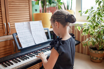 Pretty young musician in classic black dress playing digital piano at home during online concert and recording video, social distance during quarantine, online education concept, video blogging