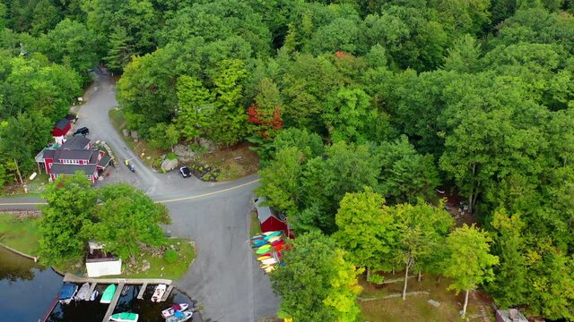 Aerial shot of boats moored at lakeshore amidst green trees, drone flying forward over harbor at lake - Berkshire County, Massachusetts