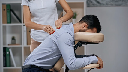 Masseur massaging back of businessman on massage chair in office