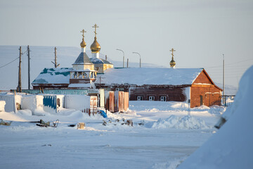 View of a snow-covered small Orthodox church in the far North of Russia in the Arctic. Church of the Transfiguration of Jesus. Anadyr, Chukotka, Siberia, Russia. Cold weather. Winter landscape.