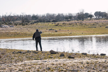 A man dressed in brown casts his fishing rod to catch fish