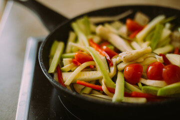 Cooking in the kitchen at home in a pan of fresh vegetables cut into strips: cherry tomato, zucchini, red pepper, eggplant