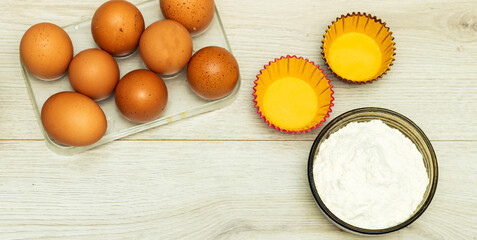 Container for eggs in clear plastic and cake mold, flour bowl on wood table