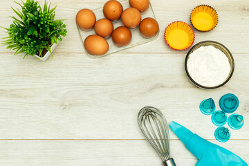 copy space with eggs and flour and Cupcake decorating tools, icing bag and nibs or tips and whip on wood table