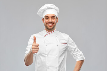 cooking, culinary and people concept - happy smiling male chef in toque showing thumbs up over grey...