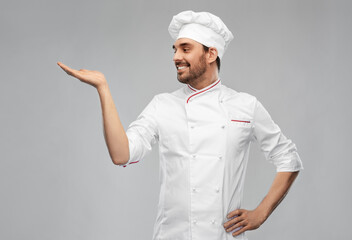 cooking, culinary and people concept - happy smiling male chef in toque holding something on hand over grey background