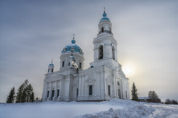 The majestic white-stone ancient church in the Ural village of Shurala (Nevyansk district, Sverdlovsk region) on a sunny winter day. Beautiful blue domes, there is a bell tower. White pure snow 