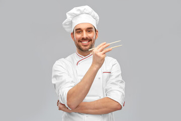 food cooking, asian cuisine and people concept - happy smiling male chef in toque holding something with chopsticks over grey background
