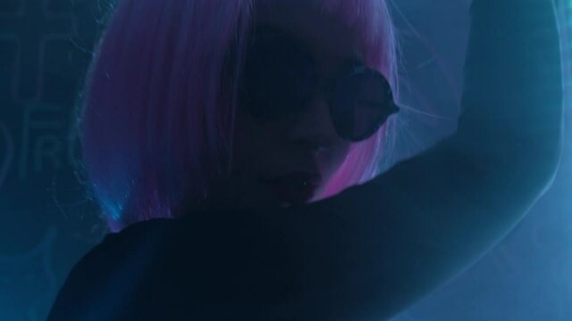 Hipster girl with glasses and a pink wig in a dark neon room with smoke.