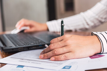 A female hand writes in a notebook near a laptop on a wooden table.