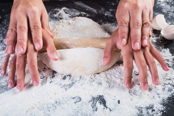 Fototapeta premium Mother and daughter hands stretching dough with a rolling pin.