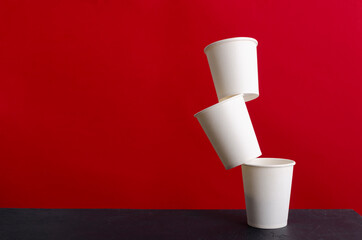 Levitation of white paper cup on the black table against red wall.Empty space