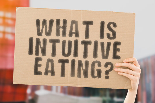 The question " What is intuitive eating? " on a banner in hand with blurred background. Food. Meal. Nutrition. Healthcare. Nutrient. Brain. Mind. Freedom. Free. Choice
