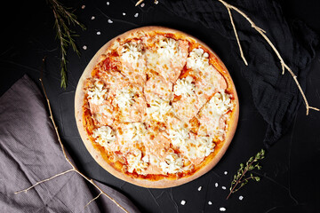 pizza on black textured background with dark napkin and golden sprigs top view