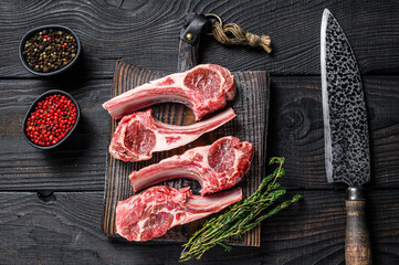 Lamb chops raw meat on bone with salt, pepper and herbs. Black wooden background. Top view