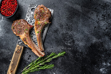 Barbecue grilled lamb chops on a butcher meat cleaver. Black background. Top view. Copy space