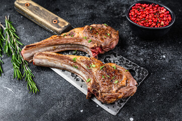 Barbecue grilled lamb chops on a butcher meat cleaver. Black background. Top view