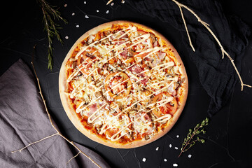 pizza on black textured background with dark napkin and golden sprigs top view