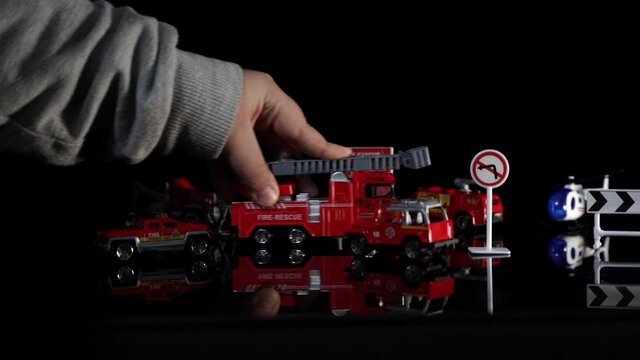 Firefighter brigade toys moved by kid's hand on black background