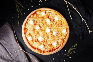 pizza on black textured background with dark napkin and golden sprigs top view