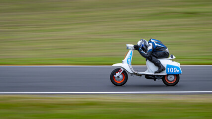A panning shot of a racing moped as it circuits a track.