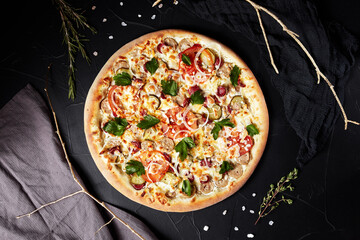 pizza on black textured background with dark napkin and golden sprigs top view