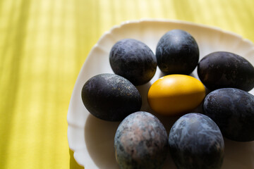 Blue painted Easter eggs and one yellow egg in a white plate on yellow background. Easter. Happy Easter 2021.
