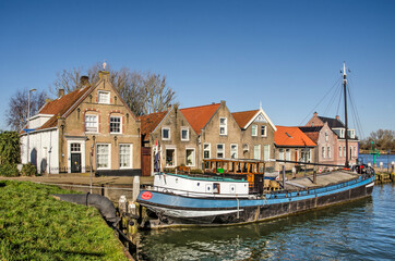 Fototapeta na wymiar Puttershoek, The Netherlands, February 26, 2021: historic houses and an inland barge in the town's small harbour with the river Oude Maas in the background