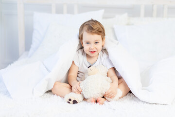 a child with a teddy bear on the bed at home plays and laughs