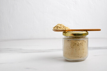 Closeup of glass jar full of mustard powder on the white table against bright wall.Empty space