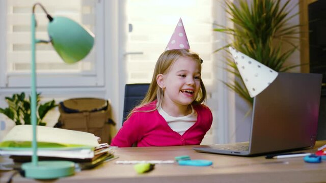 Close up birthday girl in party hat celebrates birthday alone with friends online during quarantine hold present. Pupil child internet party online communication home. Social media. Slow motion