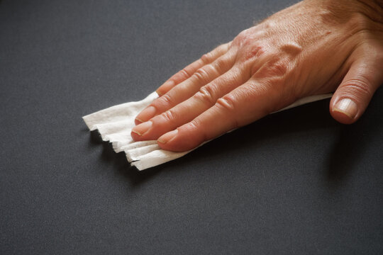 An Adult Man Wipes A Black Surface With A Damp Antibacterial Cloth. Cleaning And Disinfection