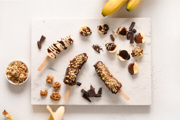 Frozen banana lollipops or lollies with walnuts sprinkles for kids on white. Easy vegan sweets. View from above.