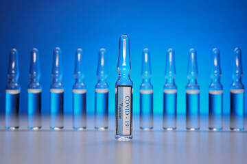 Glass ampoules with coronavirus infection vaccine lined up in a row on a blue background. Vaccination against covid-19. Immunity and health of the population. Selective focus. Ampoules with injection
