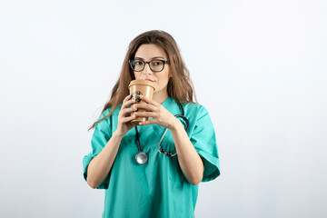 Young attractive nurse with stethoscope drinking from a cup of coffee