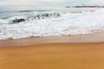 Water splashes on the coastal strip of the Mediterranean Sea with a breakwater and sandy beach in the area of San Martí in Barcelona, Spain