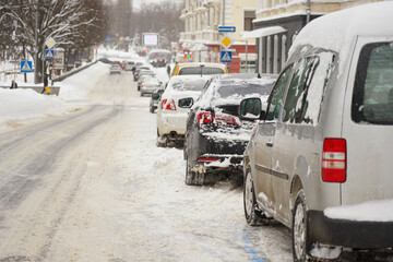 Cars stand along the street covered with snow. Cars under the snow during a heavy snowfall.