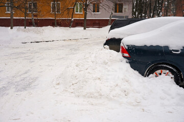 Cars stand along the street covered with snow. Cars under the snow during a heavy snowfall.