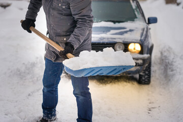 The guy is holding a shovel in his hands with snow near the car. Clearing a road for a car during a snowfall