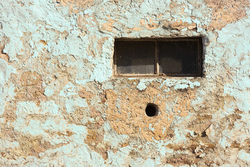 Old abandoned building with a small window and hole resembling face saying oh and paint peeling off