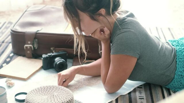Caucasian woman planning vacation travel with paper guide map at home laying relaxed on the floor - wanderlust lifestyle young female choosing next destination trip adventure 