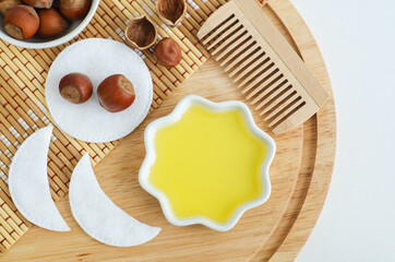 Fototapeta na wymiar Hazelnut oil in a small white bowl, wooden hair comb and cotton eye patches. Homemade face or hair mask, facial cleanser, natural beauty treatment and spa recipe. Top view, copy space.