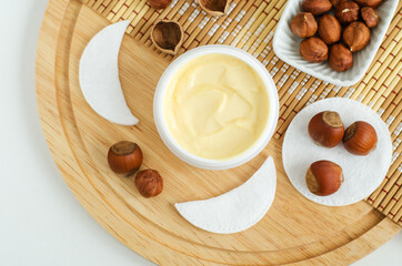 Hazelnut face cream in a small white jar and cotton pads. Homemade face mask, facial cleanser, body butter. Natural beauty treatment and spa recipe. Top view, copy space.