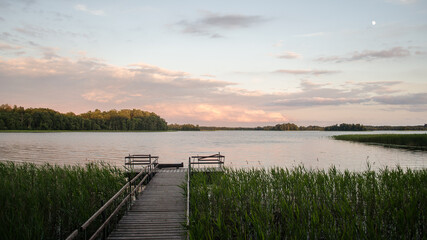 Beautiful evening view with lake Ezezers, wooden footbridge and sunlit trees, Latvia.